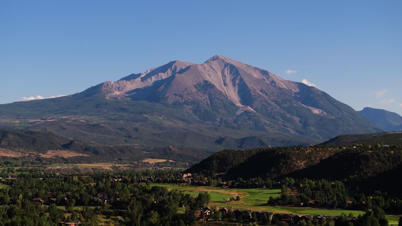 Sunlit Mount Sopris slopes glow warmly above green valleys in a wide Colorado mountain panorama, establishing static