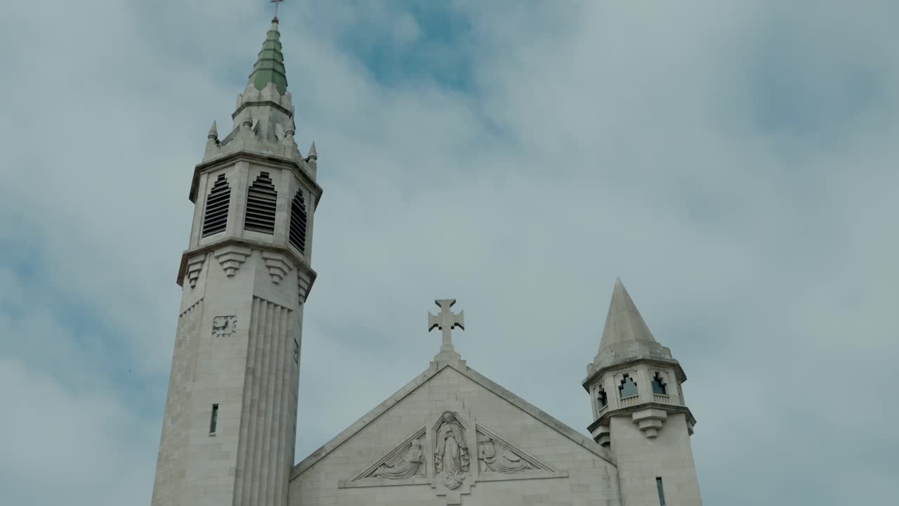 Close up of a church with two towers and a cross, set against a cloudy sky