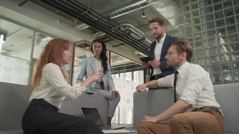 a business working group consisting of two women and two men have a relaxed meeting in the armchairs in the common area of the offices 5