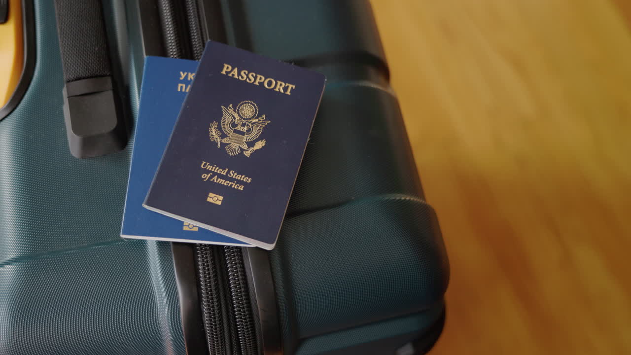 Mano che posa passaporti ucraini e statunitensi su una valigia da viaggio