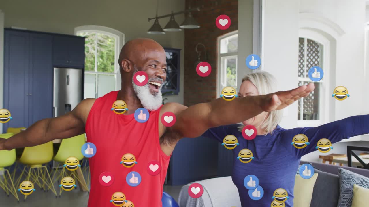 Coppia che allunga le braccia in una casa open space, facendo apparire emoji di reazione fluttuanti che celebrano il fitness.