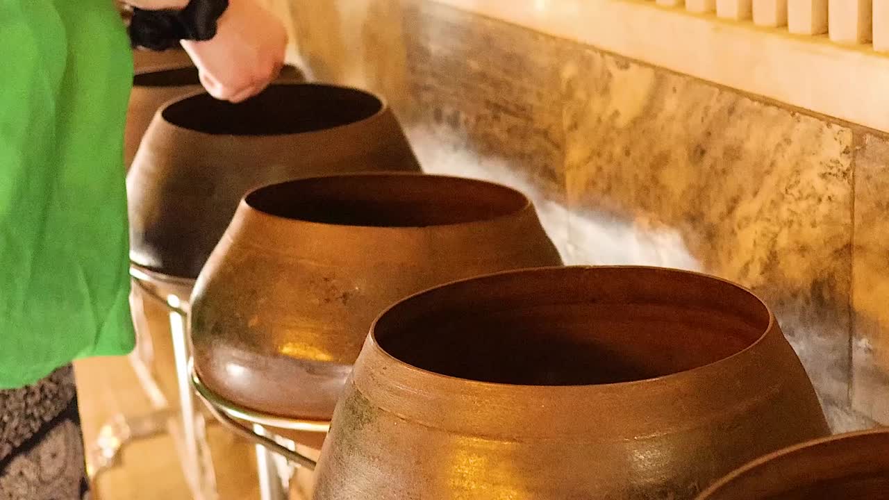 A person in a green shirt places coins into a row of bronze bowls at a temple.