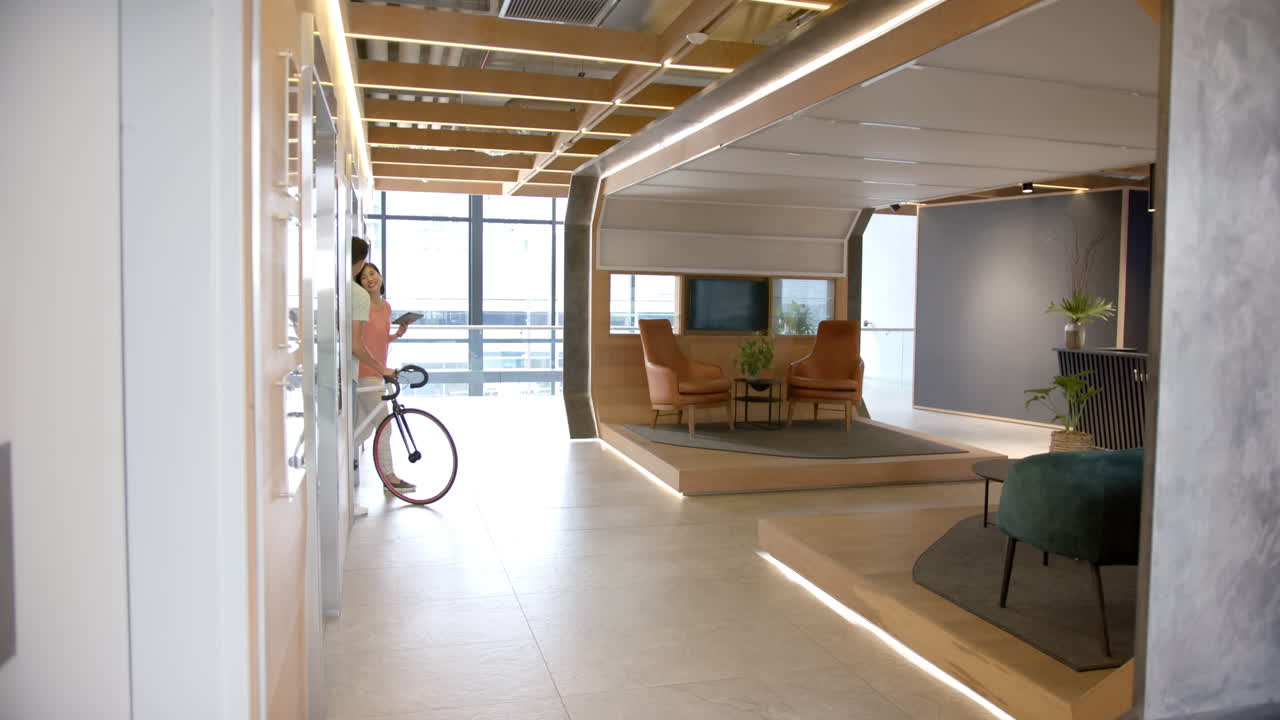 Man walking with bicycle in modern office, heading towards seating area, copy space
