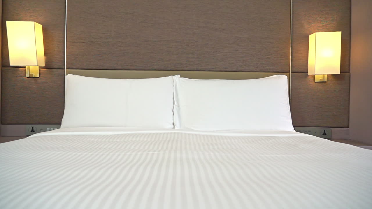 deslizándose lentamente por la habitación del hotel mostrando una cama hecha con dos almohadas blancas y luces de pared de color amarillo