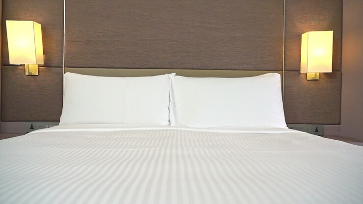 Lenta carrellata attraverso la camera d'albergo che mostra un letto rifatto con due cuscini bianchi e luci a parete di colore giallo