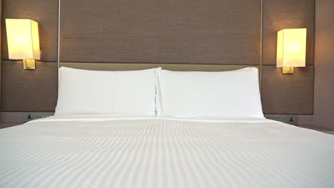 slow sliding across the hotel room showing made-up bed with two white pillows and yellow color wall lights