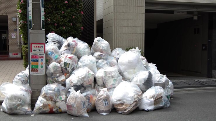 Inquadratura fissa di sacchi della spazzatura di plastica bianchi ammassati contro un palo dell'elettricità a Tokyo.