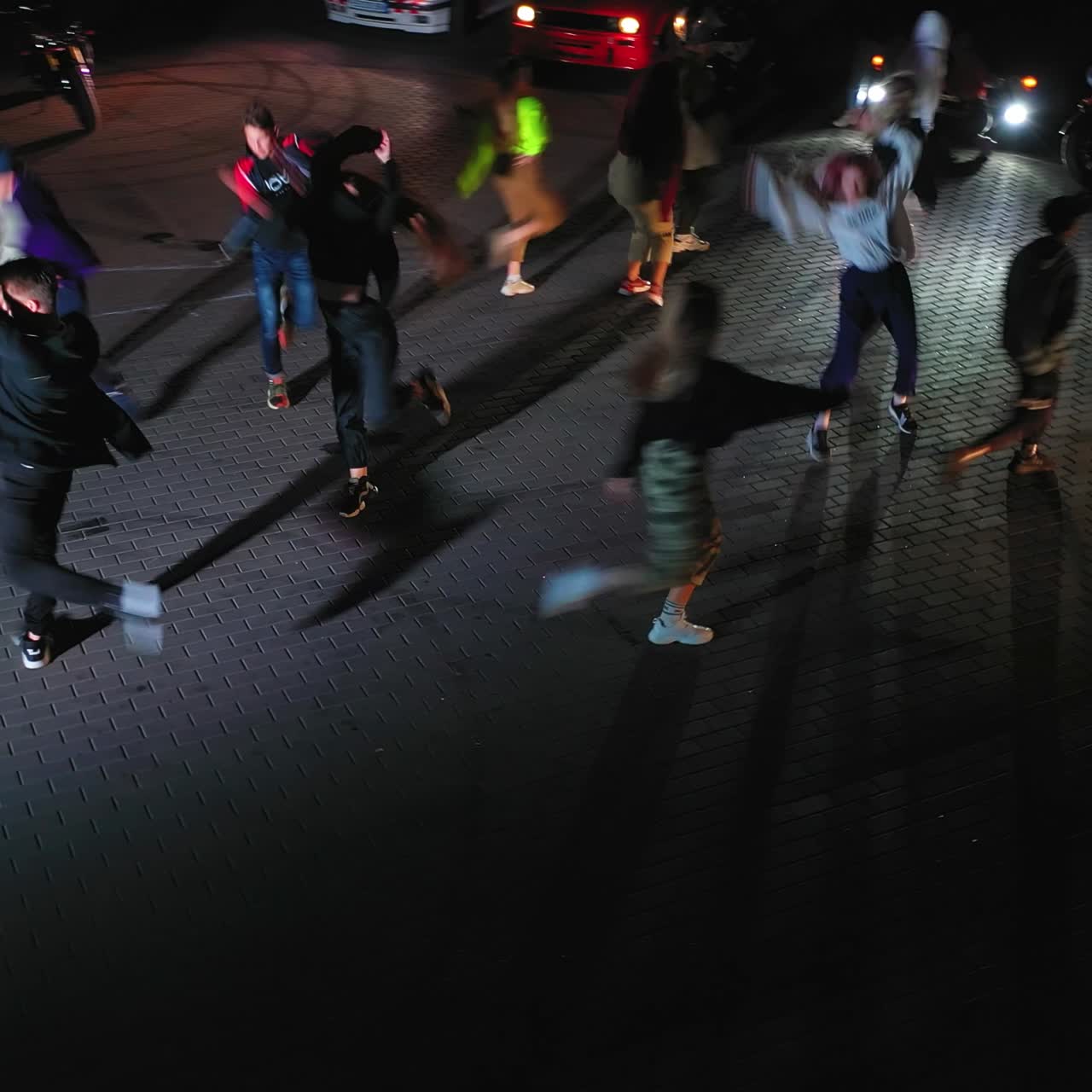 Guys dancing hip hop outdoors at night in the flashlight. Cars with headlights on standing at backdrop. View from above