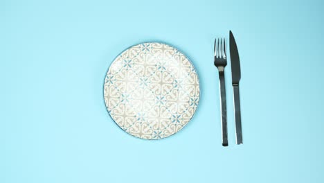 round white plate and metal fork and knife on a blue background