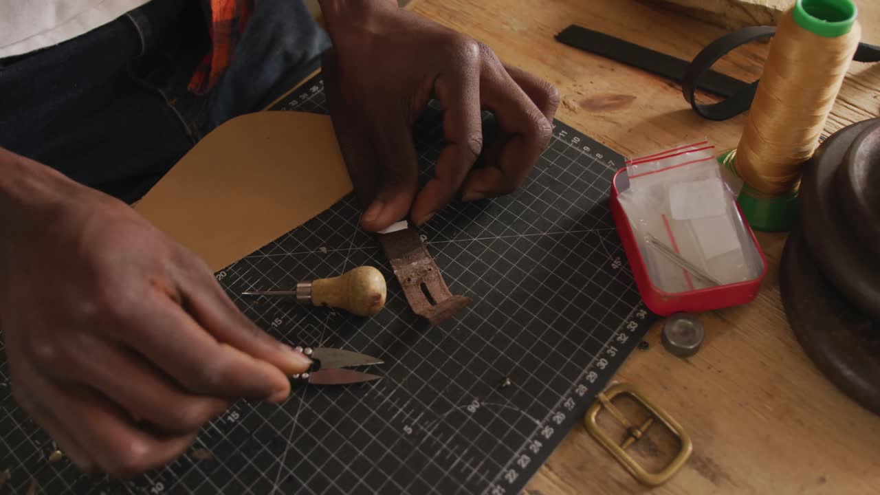 de manos artesano afroamericano preparando un cinturón en un taller de cuero