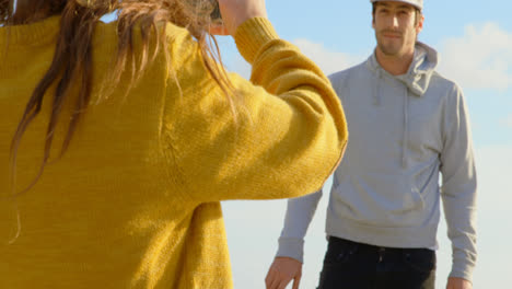 rear view of young caucasian woman clicking photo of young caucasian man with camera on the beach 4k