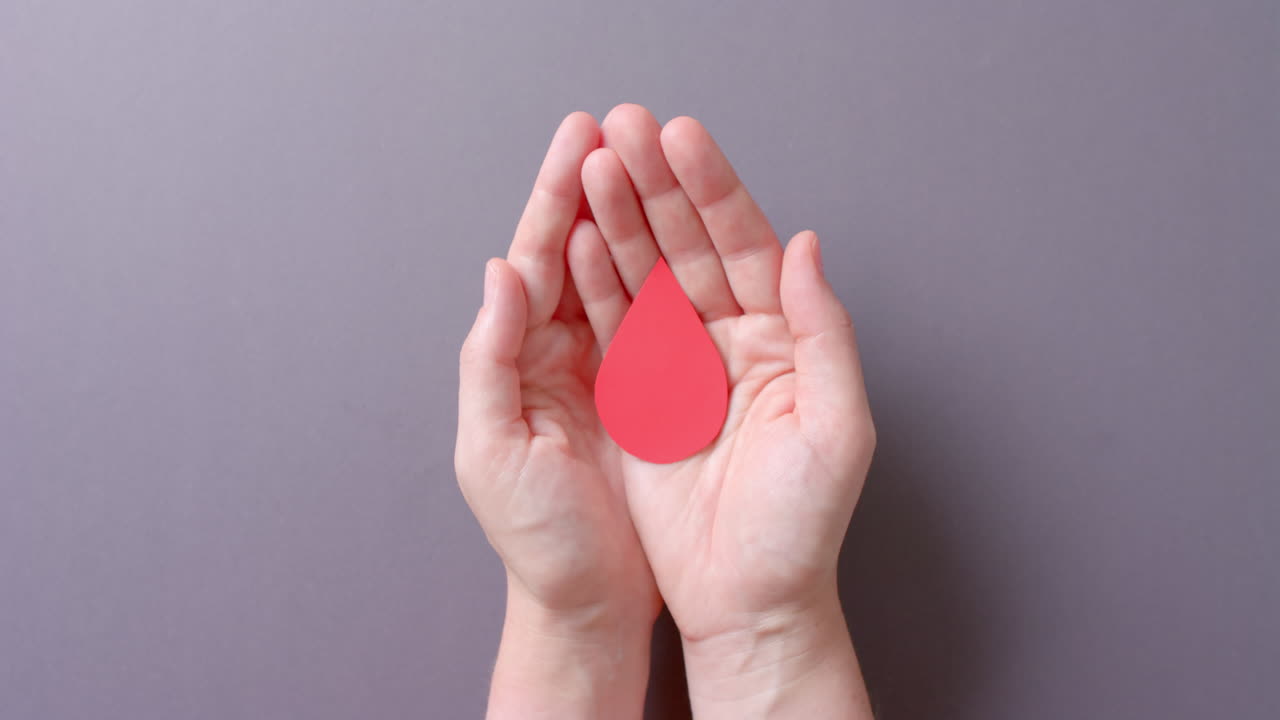 las manos de una mujer caucásica tomando gotas de sangre en un fondo gris, en cámara lenta.