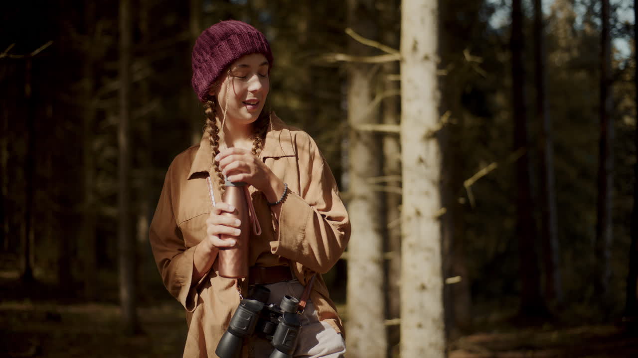 Kvinne åpner flaske stående i skogen
