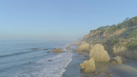 aerial shots of el matador beach over breaking waves and rocks on a hazy summer morning in malibu, california