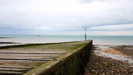 weathered wooden boardwalk jetty leading towards calm overcast ocean slow descending shot