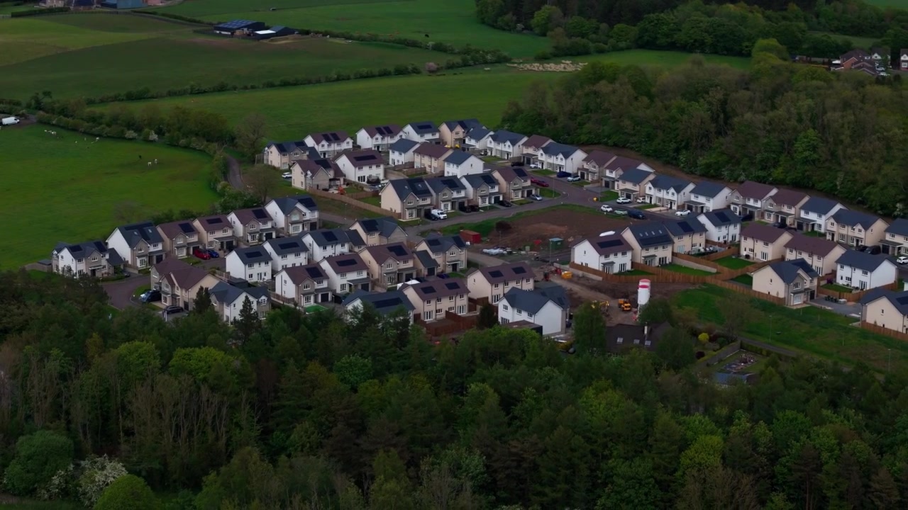 Moderne boligområde med fritliggende enfamiliehuse, pæne asfalterede veje og grønne omgivelser på den britiske landskab, aftenluftfoto