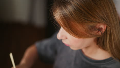 Close up of woman eating meat with chopsticks, focused expression on face, long hair falling naturally over shoulder, blurred soft indoor background