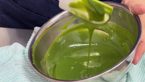 tasty sweet shiny matcha white chocolate mirror glaze making in progress, close up of a professional pastry chef hand mixing and preparing with a spatula in commercial kitchen bakery