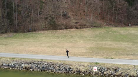 an athletic young man who starts by getting his clothes ready then jogs next to a green river along a path next to a forest