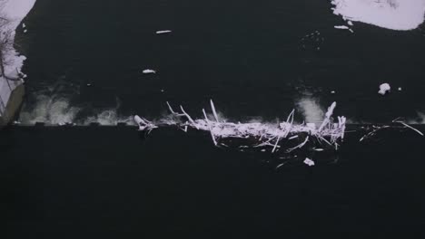 Aerial-view-of-a-dam-in-a-swift-moving-river-with-snow-covering-everything