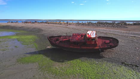 circular drone shot of a wrecked fishing boat which is rusted and lays on the beach at bahia bustamante