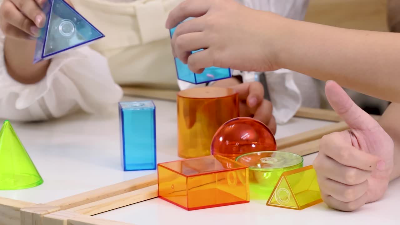 Tangan orang dewasa dan anak berkolaborasi untuk membangun menara menggunakan balok geometris 3D tembus cahaya