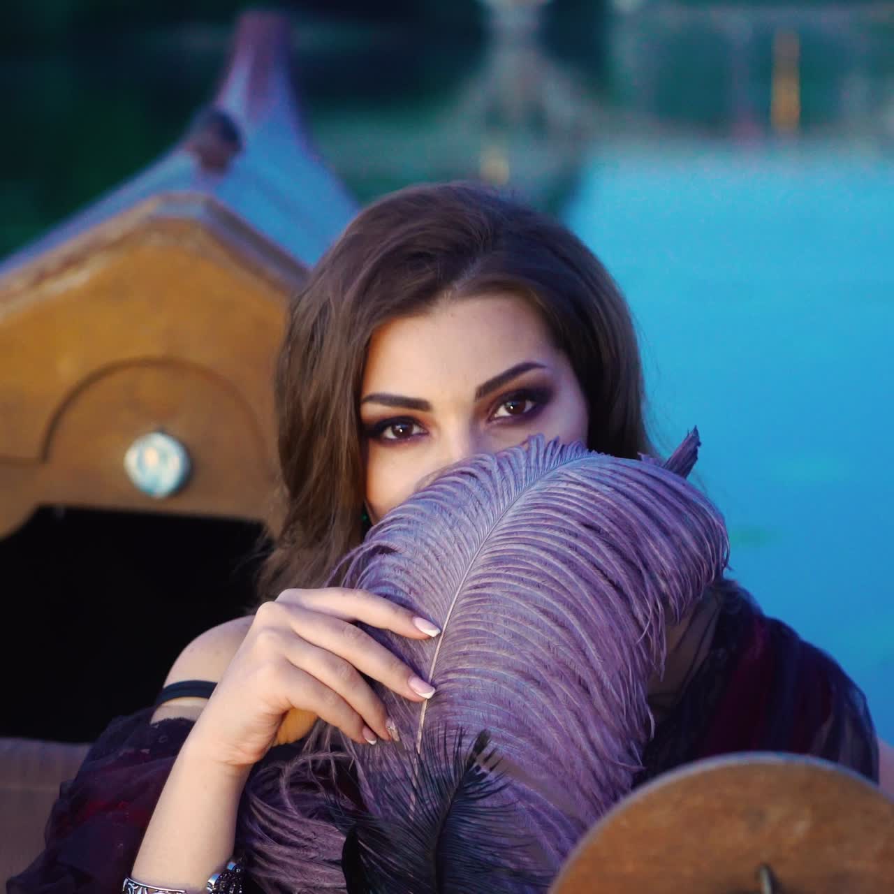 A beautiful woman playfully is glancing from under the guise of a purple feather on the gondola on a warm evening. Blurred background. Close-up