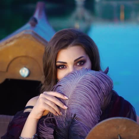 a beautiful woman playfully is glancing from under the guise of a purple feather on the gondola on a warm evening. blurred background. close-up