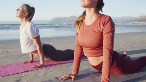 dos amigas caucásicas practicando yoga, estirándose en la playa