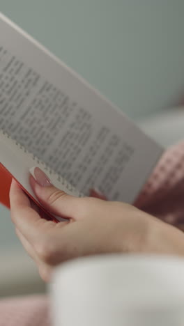 woman runs through pages of book looking for certain part of story. hands of female reader holding textbook on blurred background in room closeup