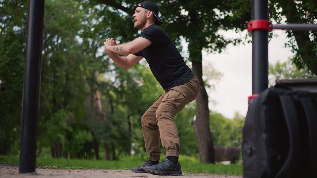Individuo che esegue correttamente lo squat, uomo che pratica lo squat profondo enfatizzando postura e controllo, uomo che esegue squat profondo preciso sul terreno del parco enfatizzando forma e coinvolgimento del core