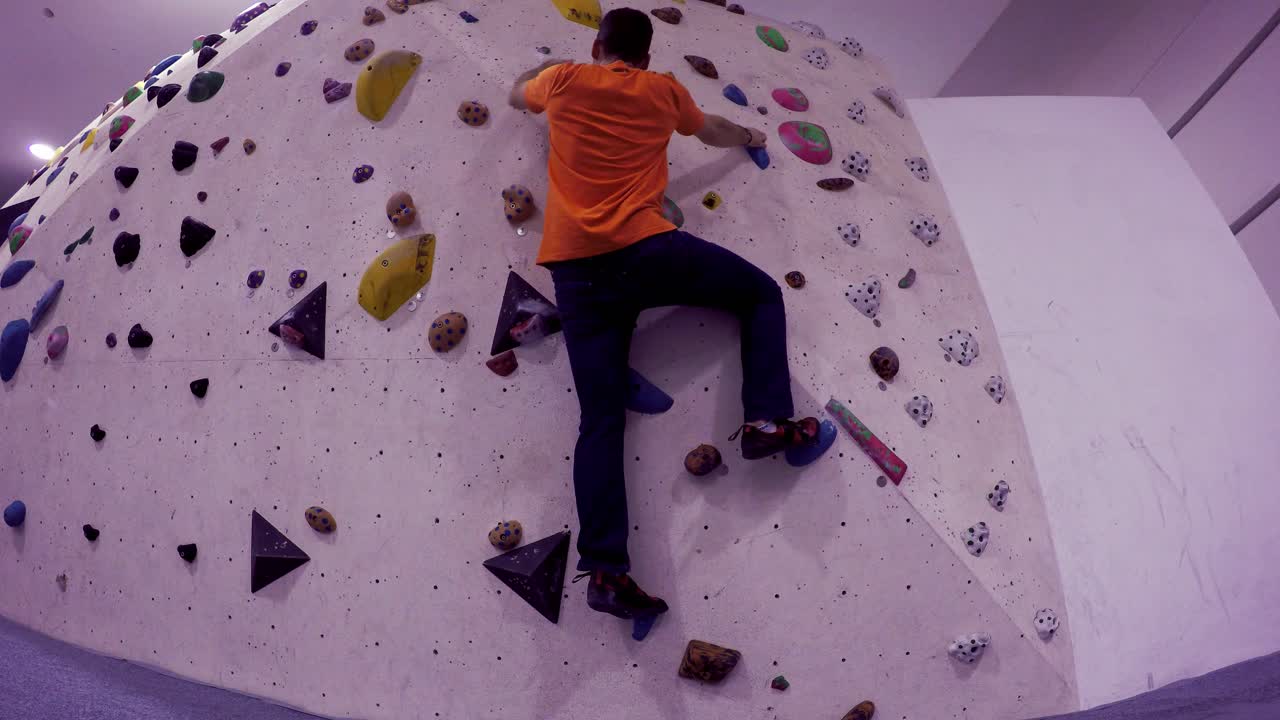 Boulder gym climbing wall seen from below as a climber approaches and climbs up and then down with no rope