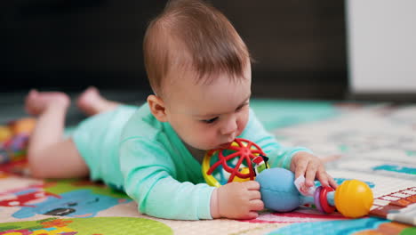 lovely child is busy with a toy. tiny boy looking carefully with his game lying on mat. close up.