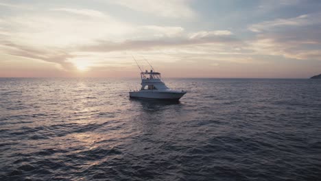semi orbit aerial of a fishing boat floating in the sea with the sun setting over the horizon in costa rica.