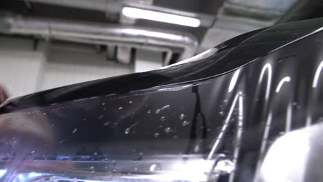 close-up pan across the front of a new car as a clear paint protection film is applied