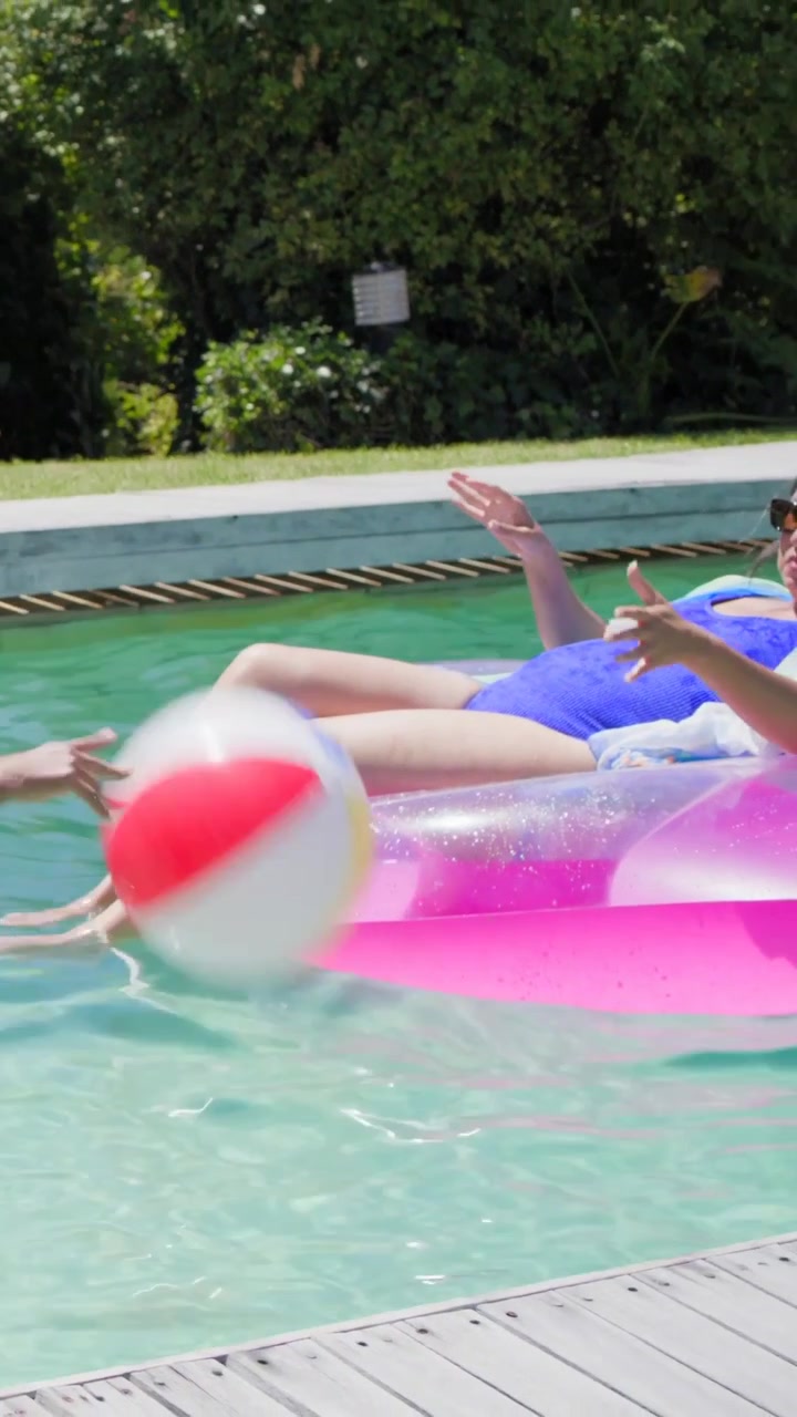 Vertical video: Tossing friend sending ball floater catching on pink ring in suit at pool for fun