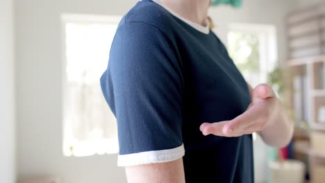 sección media de una mujer caucásica en camiseta azul marino que muestra bordes blancos en una habitación soleada, cámara lenta