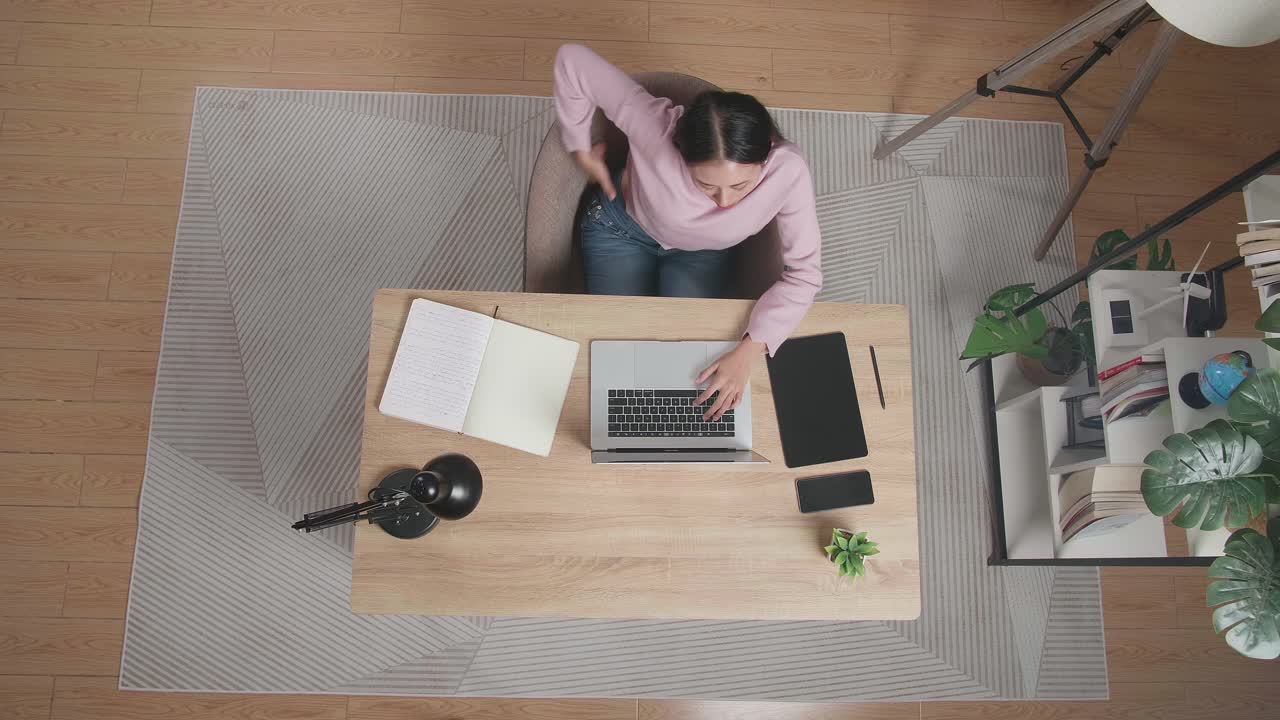집에서 노트북에 타이핑하는 나무 책상에 앉아있는 동안 스트레칭하는 여성의 상단 시각