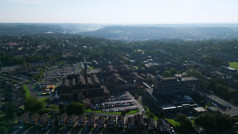 aerial footage showcases staincliff, uk, featuring industrial structures, vibrant streets, dewsbury general hospital, and the yorkshire landscape on a summer morning