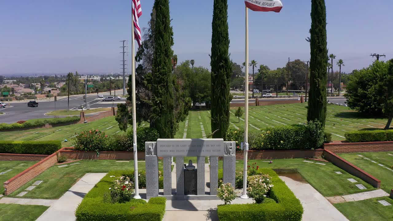 Close-up rising shot of the United States and California flags flying above a Veteran's Memorial at a mortuary in California