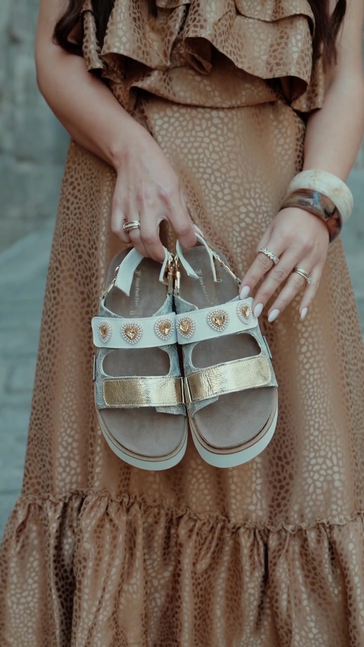 Primo piano delle mani di una donna che tengono sandali con un vestito alla luce del giorno.