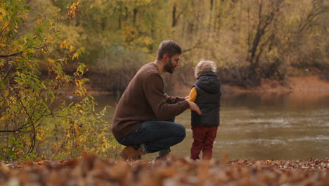 Das-Kleine-Kind-Gibt-Dem-Vater-Fünf-Und-Lacht-Gemeinsam,-Während-Es-Sich-Im-Wald-Mit-Einem-Malerischen-See-Ausruht,-Bei-Einem-Familienausflug-Und-Einer-Kommunikation-Im-Herbst