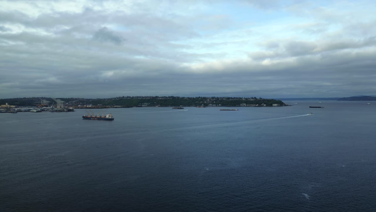 Panoramic aerial drone shot of vast ocean bay along Seattle Waterfront with cargo ships facing cloudy horizon - Seattle, Washington, USA