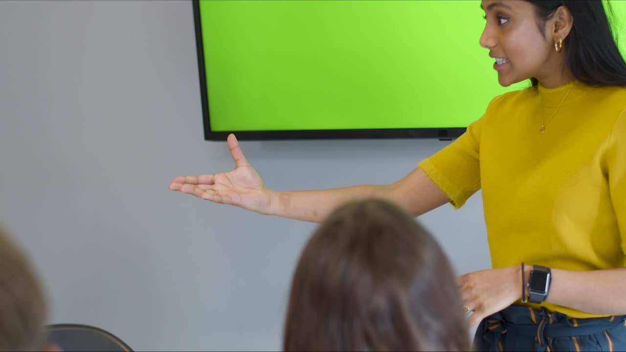 mujer sonriente presentando a sus colegas con pantalla verde tv