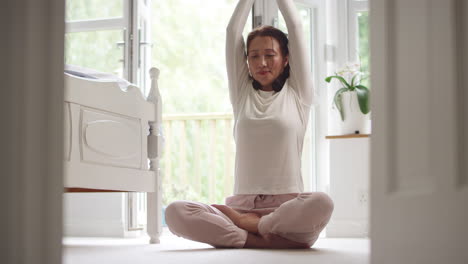 Mujer-Asiática-Madura-En-Pijama-Sentada-En-El-Suelo-Del-Dormitorio-Meditando-En-Pose-De-Yoga---Filmada-En-Cámara-Lenta