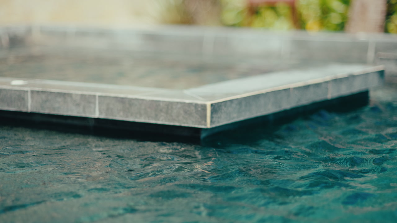 Calm blue resort pool edge with tiled infinity-style detail, gentle ripples and relaxing vacation atmosphere.