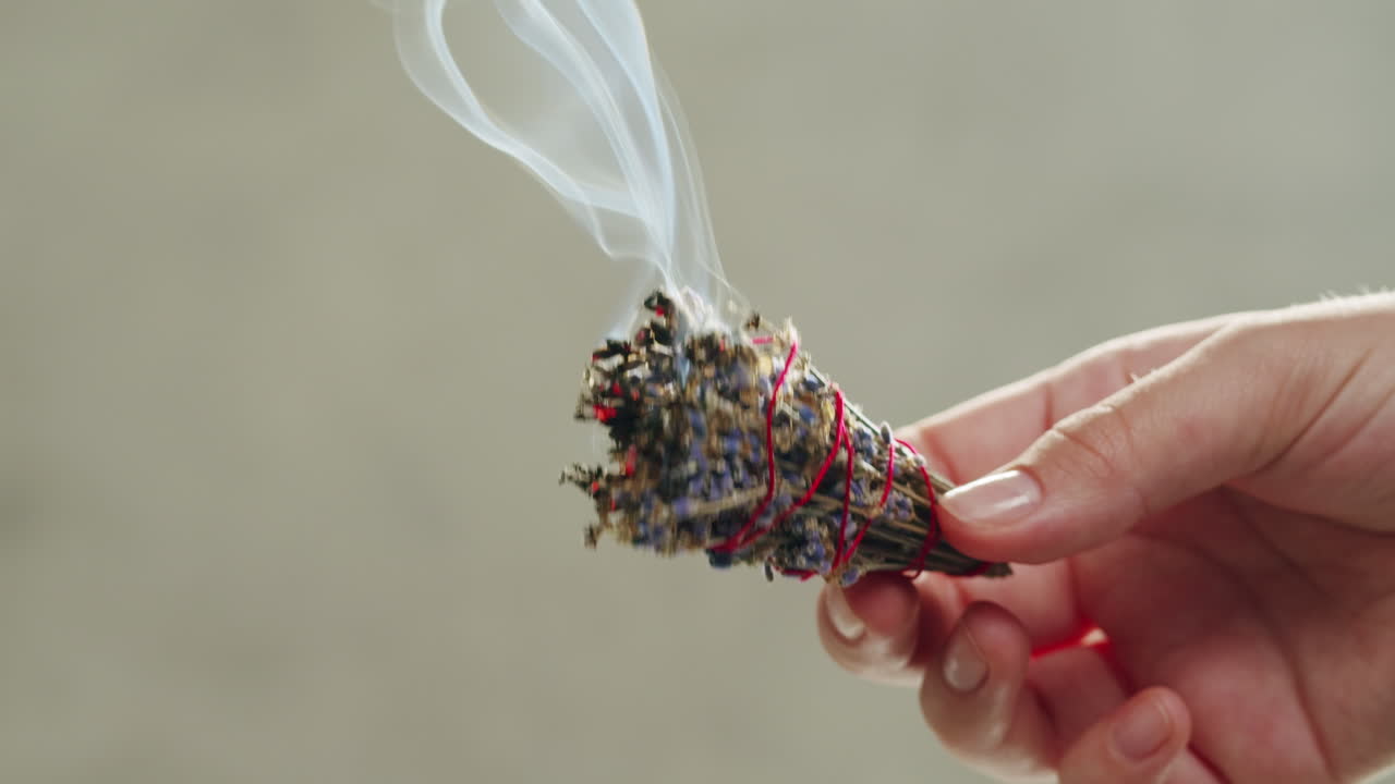 Person holding Palo Santo wood stick in hand, aromatic Palo Santo burning on black background, smoke spreading around, slow motion video clip, high quality 4k close up footage. High quality 4k footage