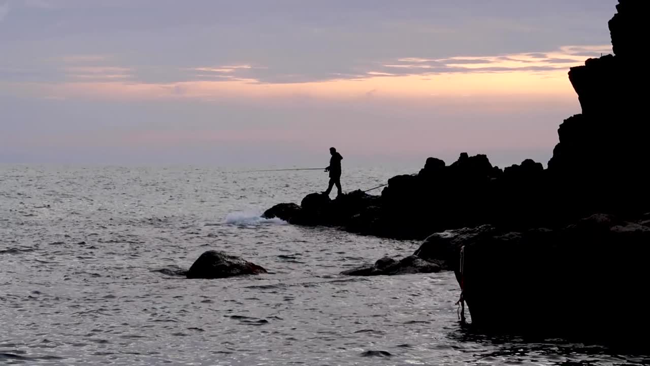hombre pescando en el mar mediterráneo al atardecer en las rocas por el pueblo italiano de cinque terre