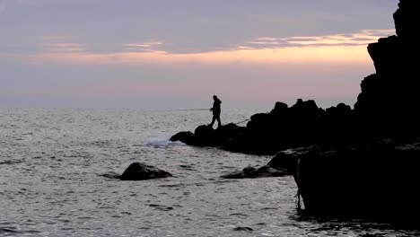 man fishing in mediterranean sea at sunset on rocks by cinque terre italian village