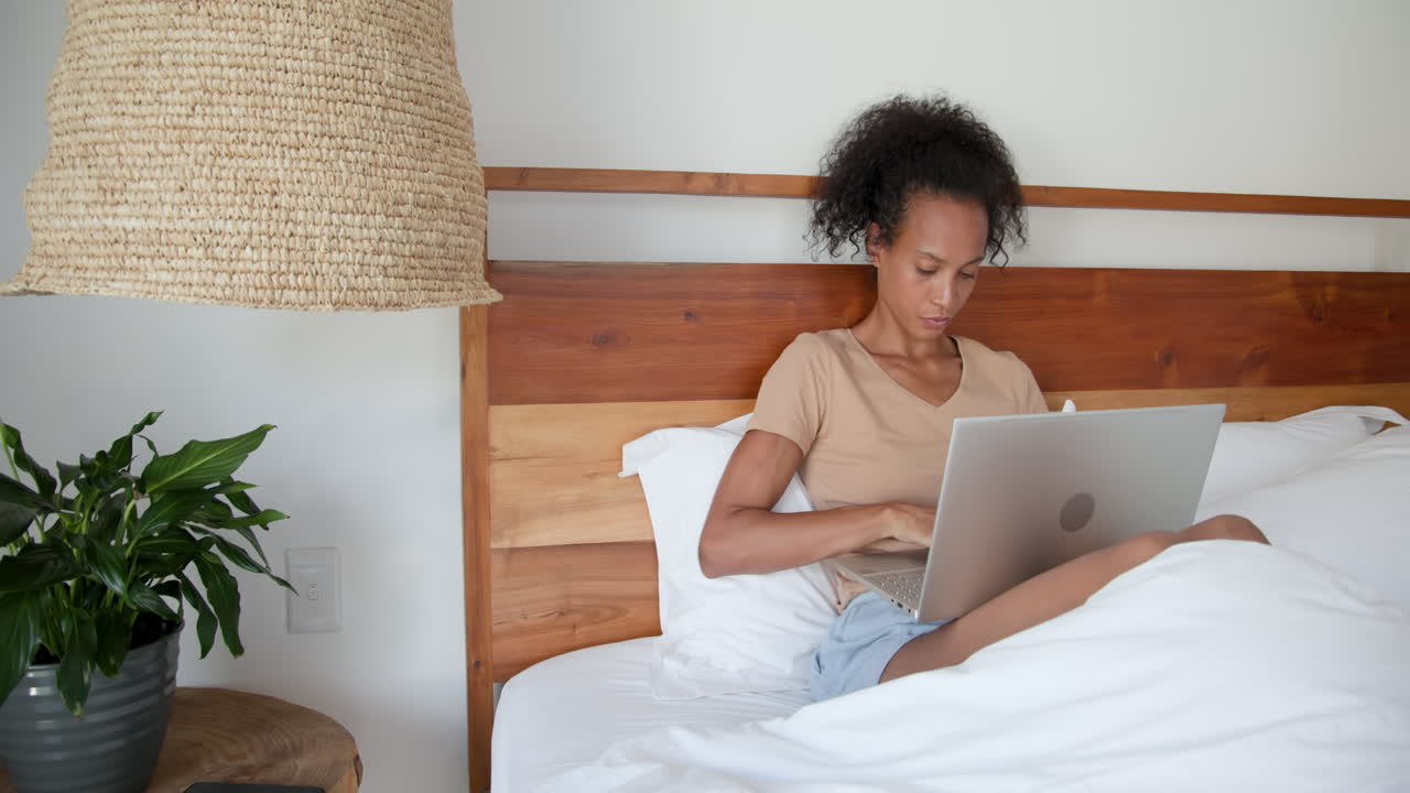 woman working on laptop in bed, focused and productive, at home